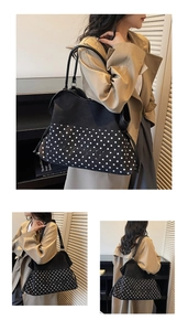 Close-up of black and white polka dot tote bag with leather handles and cursive logo