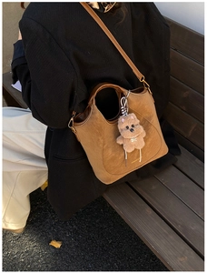 Close-up of caramel faux suede tote bag with plush bear charm on a park bench