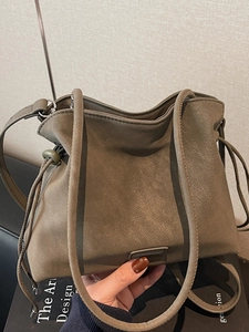 Brown suede drawstring bucket bag with elegant metal logo and slim leather shoulder strap