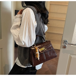 Detail of dark brown glossy leather handbag with gold metal lock and wood bead charm