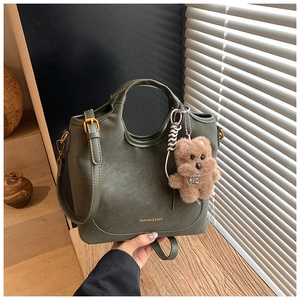 Detail of olive green faux leather bucket bag featuring gold text and brown bear charm