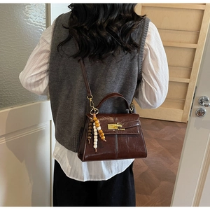 Detail view of brown leather handbag with gold twist lock and colorful bead tassel