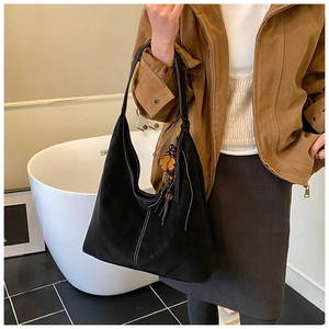 Détail d'un sac cabas noir mat avec coutures contrastées et pendentif fleur à franges