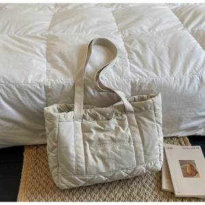 Detail of beige quilted tote bag showing padded rhombus pattern and white embroidery