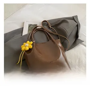 Detail of a brown leather shoulder bag featuring a yellow crochet flower charm and handle