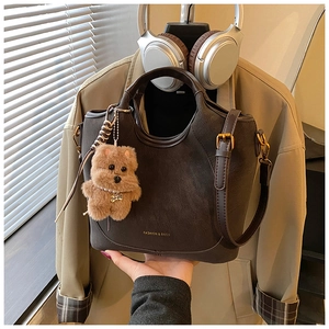 Detail of dark coffee vintage bucket bag with plush bear charm and gold lettering
