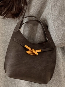 Borsa a secchiello grigio-marrone con chiusura dorata indossata su maglione lavorato