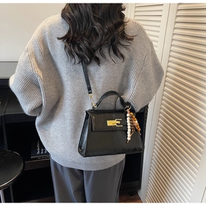 Detail of a black structured crossbody bag with gold hardware and beaded wooden charm