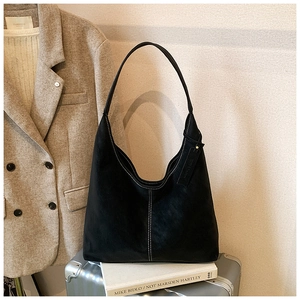 Détail du sac hobo en daim noir avec surpiqûres blanches sur une valise argentée