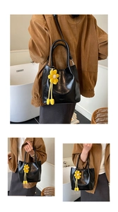 Detail of black glossy PU bucket bag with a yellow knit flower charm and embossed logo