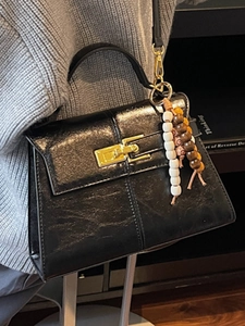 Fashionable black faux leather crossbody bag with gold buckle and beaded charm detail