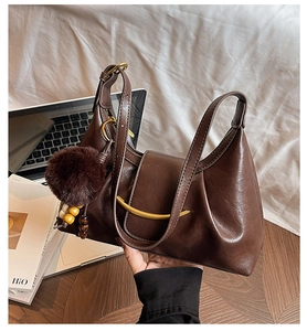 Detail of dark brown leather tote with gold hardware and plush ball charm on a bag