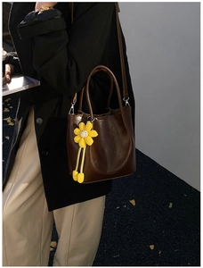 Deep brown bucket bag with woven sunflower charm shown in a stylish street setting