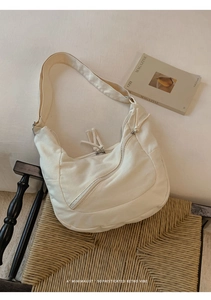 Close-up of a minimalist cream canvas hobo bag with a zipper pocket on a woven chair