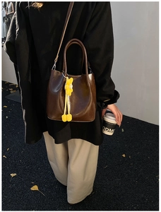 Detail of dark brown leather bucket bag with elegant yellow flower charm and top handle