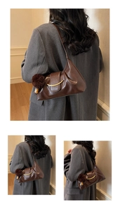 Close-up of dark brown hobo bag with gold metal trim, pom-pom charm and wood bead detail