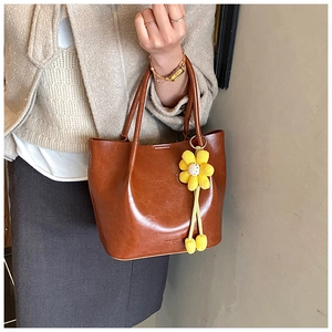 Detail of dark brown polished leather bucket bag with a yellow knitted sunflower charm