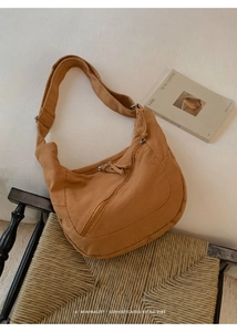 Close-up of caramel canvas crescent shoulder bag on a vintage woven chair with magazines