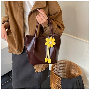 Detail of a dark brown glossy leather tote bag featuring a yellow knitted daisy charm