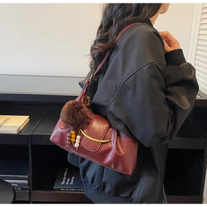 Detailed close-up of dark red pleated leather shoulder bag with gold metal trim and charms