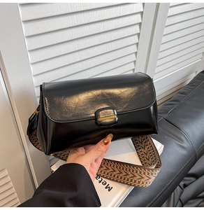 Detail of black glossy shoulder bag with golden buckle and geometric woven strap