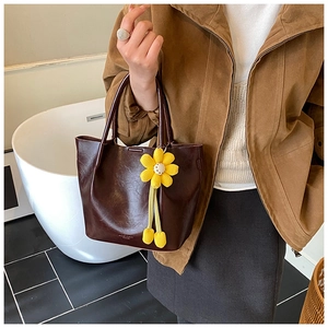 Detail of a brown leather bucket bag with a vibrant yellow sunflower woven pendant charm