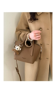 Dettaglio borsa a secchiello in pelle marrone con ciondolo orso su cappotto color cammello