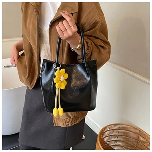 Detail of glossy black bucket bag with a yellow knitted sunflower charm on a handle