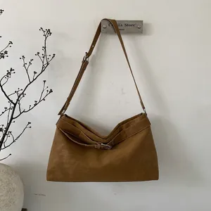 Close-up of brown suede shoulder bag with decorative buckle and matte texture