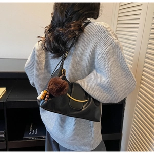 Detail of minimalist black leather half-moon shoulder bag with gold metal trim and fuzzy charm