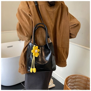 Close-up of black leather bucket bag with a decorative yellow sunflower charm detail