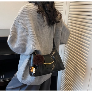 Detail of black leather shoulder bag with gold crescent hardware and fuzzy ball charm