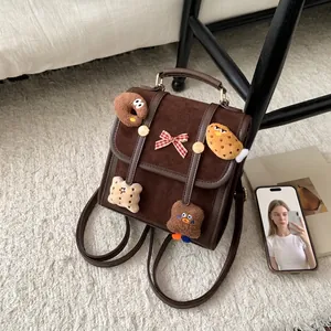 Detail of a dark brown suede mini backpack with cute cookie plush charms and a red bow