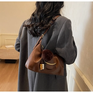 Detail of dark brown leather underarm bag with gold crescent buckle and plush charm