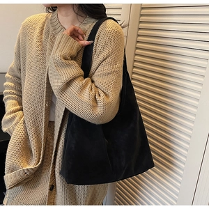 Close-up of black suede tote bag with wide shoulder strap worn by a woman