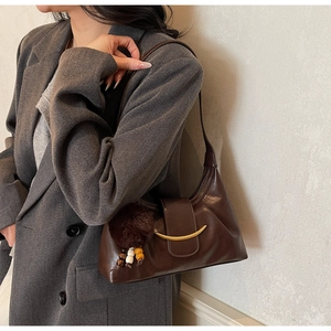 Detail of dark brown leather hobo bag with gold crescent buckle and plush charm on tweed suit