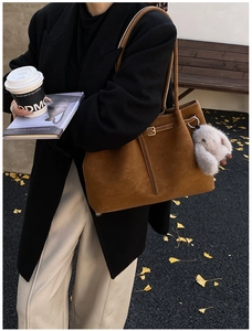Close-up of caramel brown suede tote bag with a plush rabbit charm and metal buckle detail