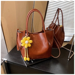Detail view of vintage brown leather bucket bag with yellow floral charm on book prop