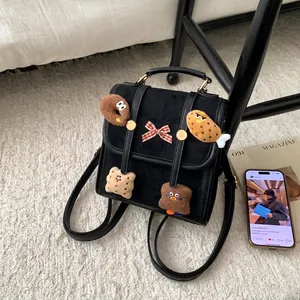 Detail of a black suede backpack featuring cute plush charms and a plaid bow decoration