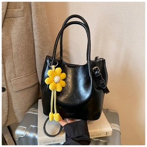 Detail of black glossy bucket bag with yellow flower charm on silver suitcase