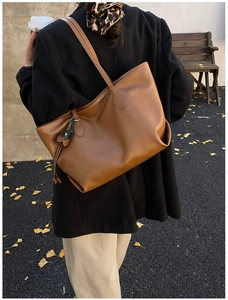 Detail of minimalist brown leather tote bag with flower pendant on autumn leaves background