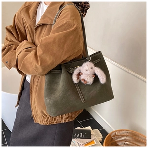 Detail of dark green matte tote bag with grey rabbit plush pendant and fine stitching