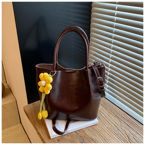 Deep burgundy leather bucket bag with top handles and floral charm on a wooden bench