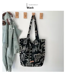 Détail du sac fourre-tout en peluche avec motifs paisley noirs et patch logo en cuir brun