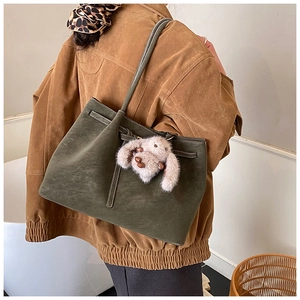 Detailed close-up of dark olive tote bag with leather straps and plush bunny charm