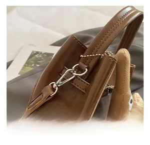 Dettaglio della borsa in pelle lucida marrone con ganci in metallo e charm