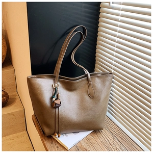 Detail view of large brown tote bag with leather texture and stylish ball tassel decoration