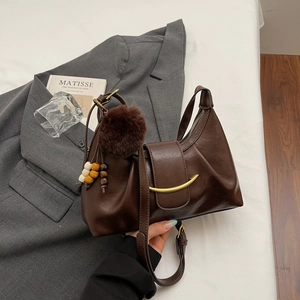 Close-up of brown leather dumpling bag with textured pleats and decorative fur ball charm