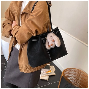Close-up of black tote bag featuring contrast white stitching and plush bunny charm