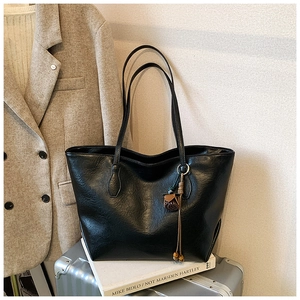 Detailed macro view of black glossy leather tote bag with vintage flower tassel accessory